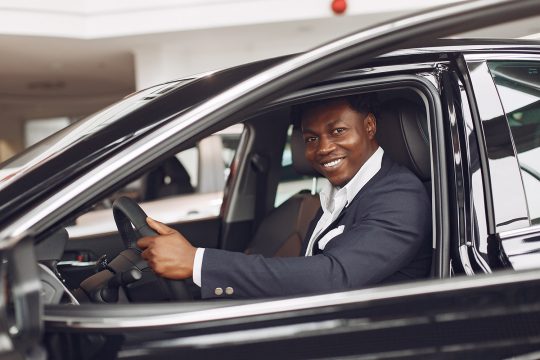 Man buying the car. Businessman in a car salon. Black male in a suit.